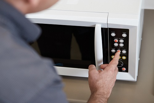 A man presses a button on a microwave marked with tactile identifiers