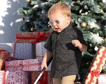 Image show VA child client Parker in front of a Christmas tree and using his white cane
