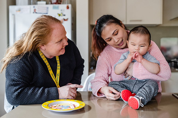 Nicholas is sitting at the kitchen eating himself with the support of his mother and Vision Australia's early childhood specialist teacher 
