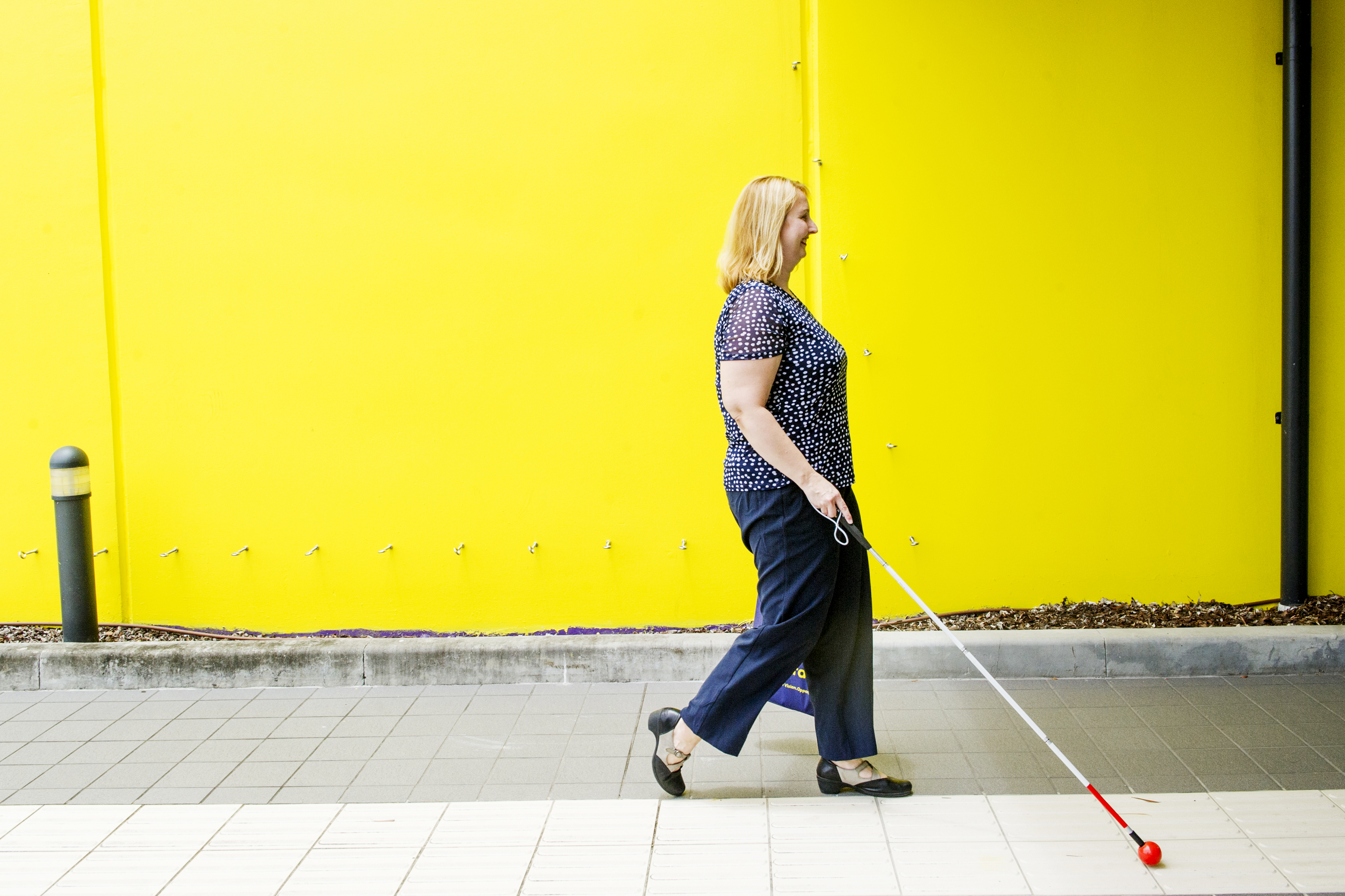 Woman walks on a footpath with her white cane in front.