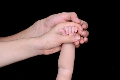 Image shows two adult hands holding a child's hands