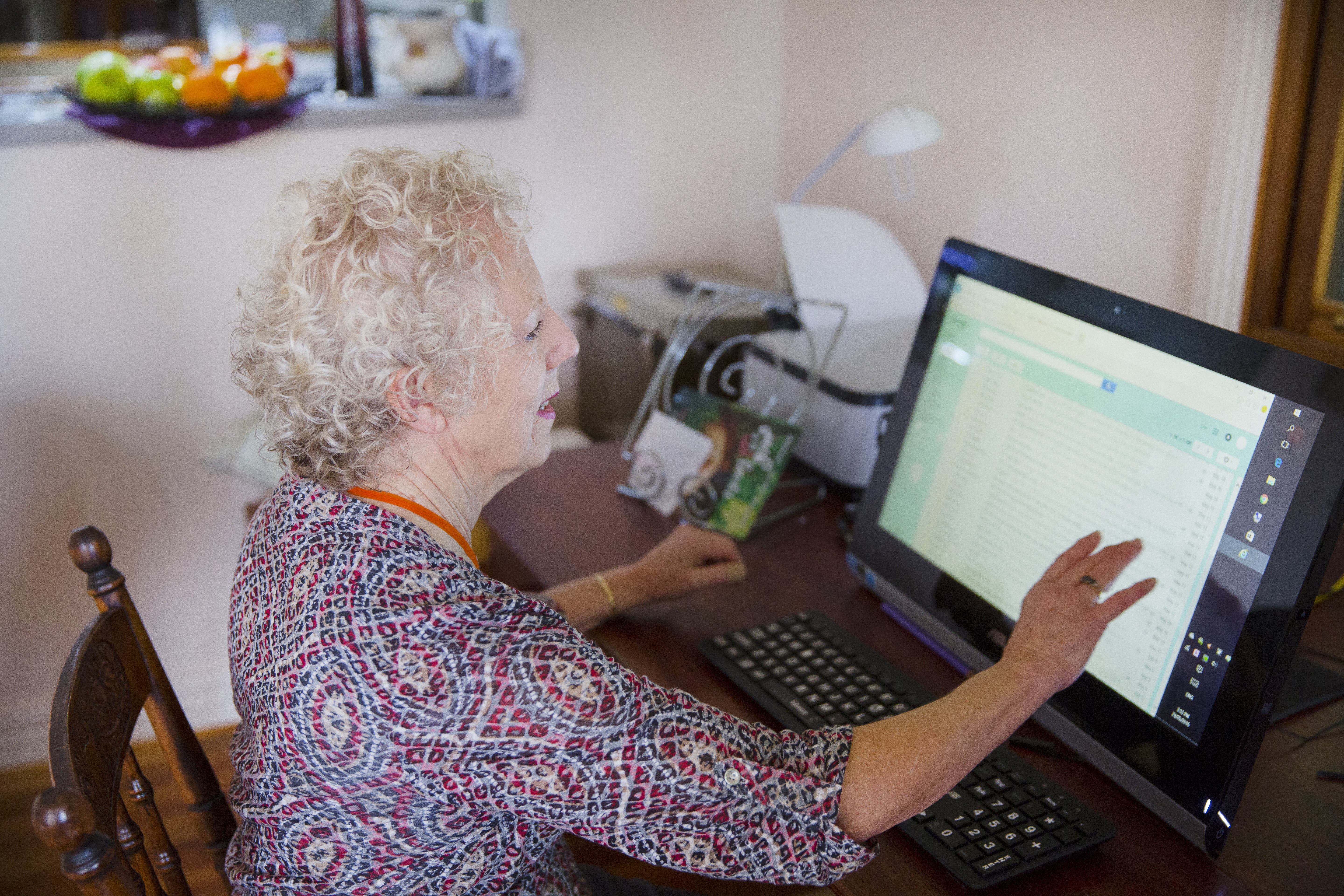 Woman using a computer with magnification software and large print keyboard, next to her is a printer 